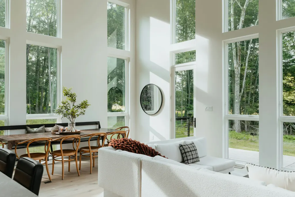 The living room of Forest House, with tall windows onto the forest and a white sofa