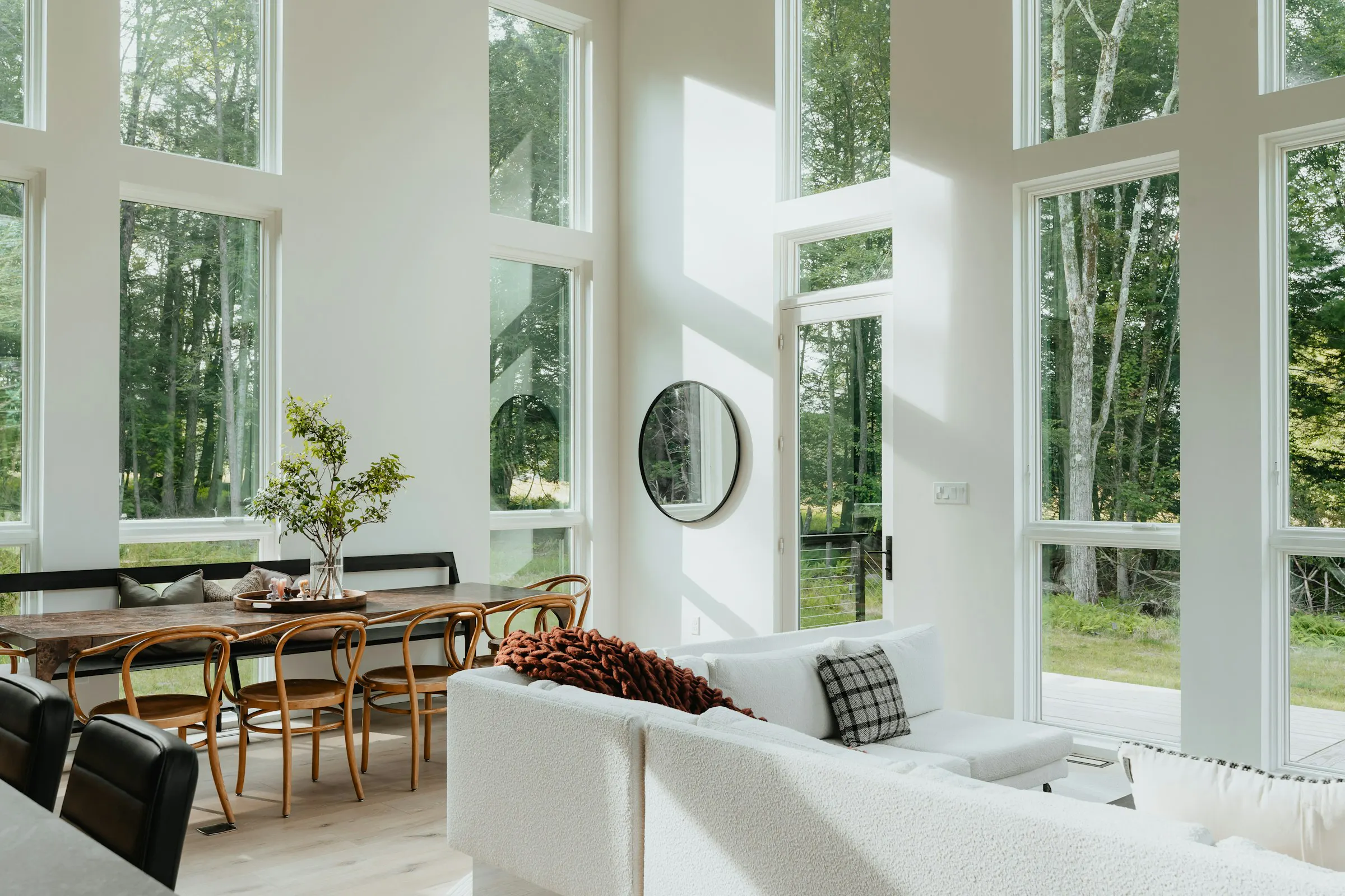 The living room of Forest House, with tall windows onto the forest and a white sofa