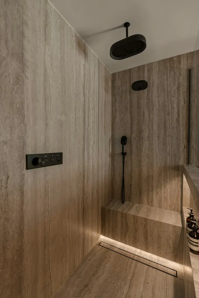 A shower in stone tiles, with a bench