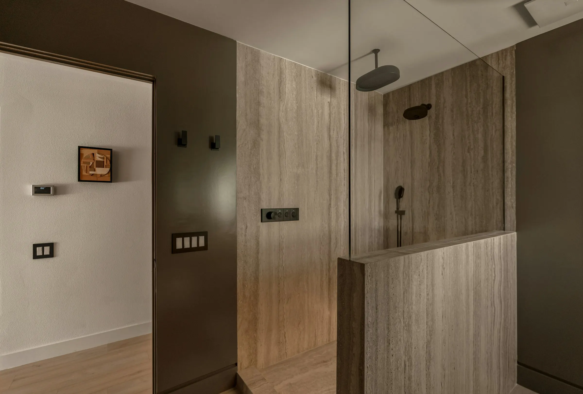 A bathroom with a glass shower enclosure in travertine